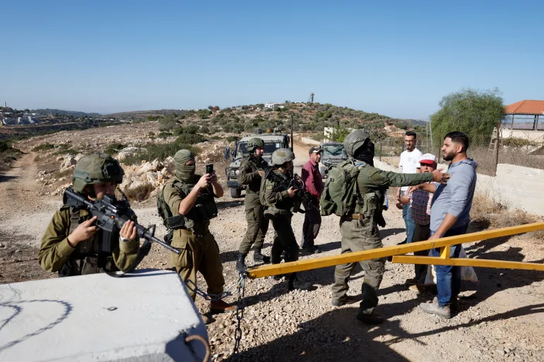 جنود من قوات الاحتلال الإسرائيلية يمنعون فلسطينيين من الوصول إلى أشجار الزيتون (رويترز)