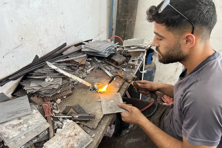 فني يصلح جسور الألواح الرصاصية لوصلها ببعضها لتركيب خلايا البطارية وإعادة تشغيلها (الجزيرة)