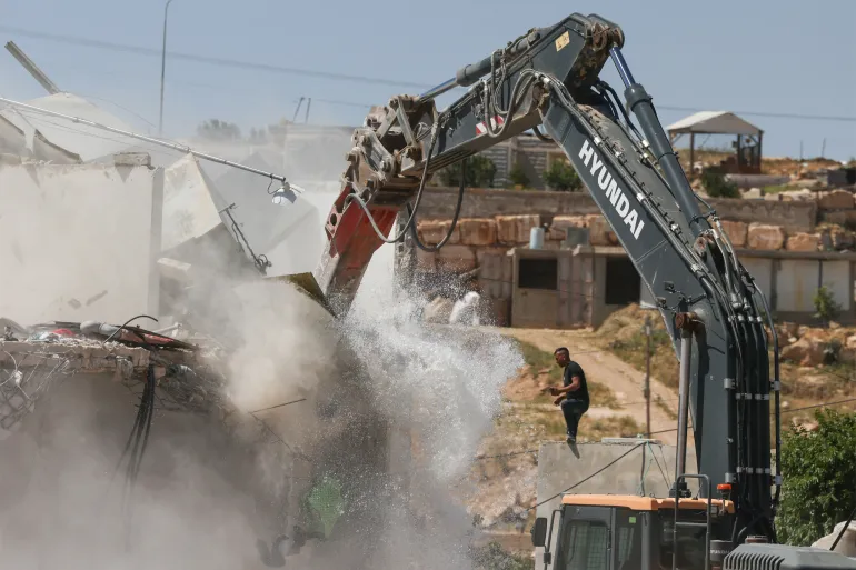 جرافة إسرائيلية تهدم منزلا فلسطينيا بحجة البناء دون ترخيص قرب بلدة يطا في مدينة الخليل بالضفة الغربية (الفرنسية)