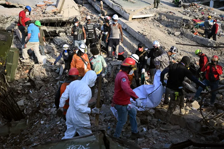 عمال إنقاذ يحملون جثث ضحايا انتشلوها من تحت أنقاض الزلزال في فنزويلا (الفرنسية)