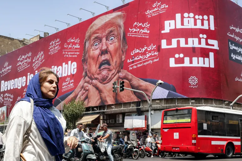 امرأة تسير أمام لوحة إعلانية كبيرة في وسط طهران تتعهد بالانتقام من الرئيس الأمريكي دونالد ترمب (الفرنسية)