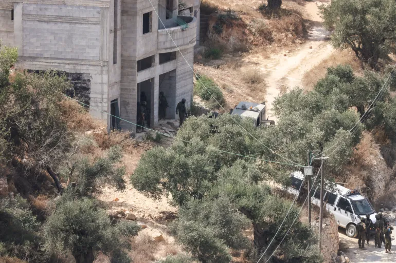 جنود إسرائيليون في موقع الهجوم الذي شنه مستوطنون على منزل فلسطيني في قرية قصرة شمال الضفة (الفرنسية)